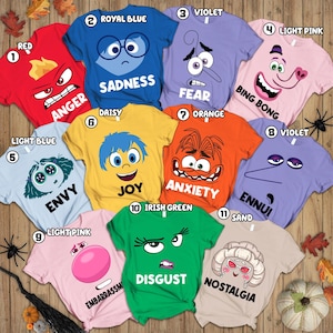 May include: A collection of eleven colorful t-shirts, each featuring a different character and emotion from the animated film. The shirts are in various colors, including red, blue, and green, with text labels like "Anger" and "Sadness".