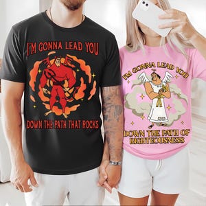 May include: Black and pink graphic t-shirts. The black shirt features a cartoon devil with the text "I'M GONNA LEAD YOU DOWN THE PATH THAT ROCKS." The pink shirt has an angel graphic and reads "I'M GONNA LEAD YOU DOWN THE PATH OF RIGHTEOUSNESS."