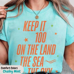 May include: A light blue t-shirt with the text "KEEP IT 100 ON THE LAND THE SEA" in orange. The shirt has a crew neck and short sleeves. The shirt is a Comfort Colors Chalky Mint.
