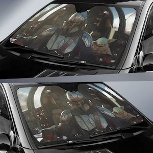 May include: Car windshield sunshade featuring a detailed image of The Mandalorian and Grogu from the Star Wars series. The sunshade is black and covers the entire windshield, offering protection from the sun.