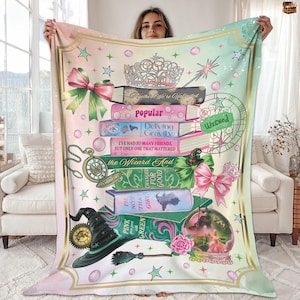 May include: A colorful blanket featuring a stack of books with titles like "Popular" and "Defying Gravity." The design includes a witch's hat, a crystal ball, a bow, and a crown. The blanket has a pink, green, and gold color scheme with text that reads "Together We're Walticated."