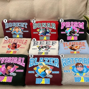 May include: A collection of nine sweatshirts in various colors, each featuring a unique graphic design and text. The designs include cartoon characters and the text "ROBERT", "SONAR", "PRISM", "MALEVOLA", "BEEF", "FLAMBAE", "INVISIGAL", "BLAZER", and "WATERBOY".
