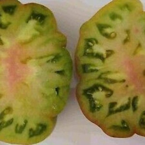 Könnte beinhalten: Zwei Hälften einer grünen Tomate mit einem rosa Kern und grünen Adern. Die Tomate ist halbiert und das Innere ist sichtbar.