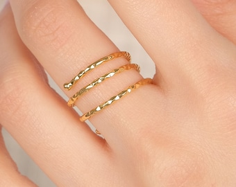 May include: A gold-toned ring featuring a triple-band design with a textured, faceted surface. The ring consists of three thin, parallel bands that wrap around the finger, creating a layered appearance with a reflective, metallic finish.