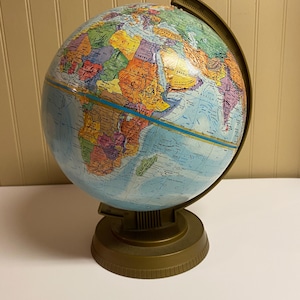 Może przedstawiać: Kolorowy, zabytkowy globus z szczegółową mapą świata. Globus przedstawia niebieskie oceany i kontynenty w różnych kolorach, zamontowany na podstawie i pierścieniu południkowym w kolorze brązu. Klasyczny przedmiot edukacyjny lub dekoracyjny.