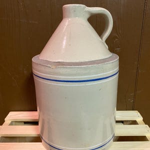 May include: A white ceramic jug with a blue and white striped design. The jug has a handle and a wide mouth.