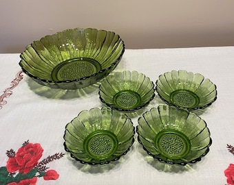 May include: A set of five green glass bowls. The large bowl has a scalloped edge and a textured center. Four smaller bowls with similar designs are arranged around the large bowl. The bowls are made of transparent green glass.