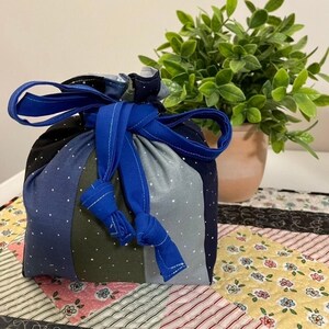 May include: A blue and green fabric drawstring bag with white polka dots. The bag is tied with a blue ribbon and is sitting on a patterned surface.