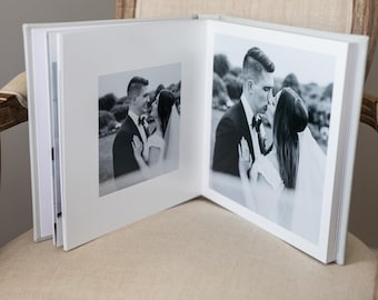 May include: A white wedding album with a black and white photo of a couple kissing on the front cover.