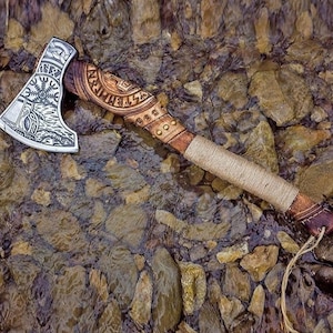 May include: A silver axe with a wooden handle. The axe head is decorated with intricate carvings and runes. The handle is wrapped in brown leather and has a braided rope attached to the end.