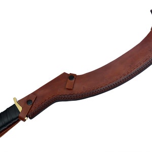 May include: A brown leather scabbard with a curved blade and a gold-colored handle. The scabbard has decorative stitching and a snap closure.