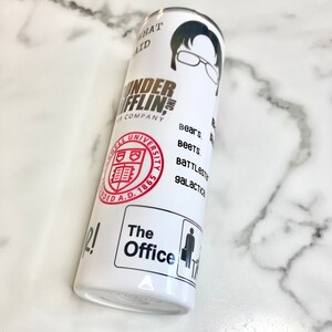May include: White tumbler with a black and white image of a man wearing glasses. The text "Dunder Mifflin" is printed in gold on the tumbler. The text "Bears. Beets. Battlestar Galactica" is printed in black on the tumbler. The text "The Office" is printed in black on the tumbler.