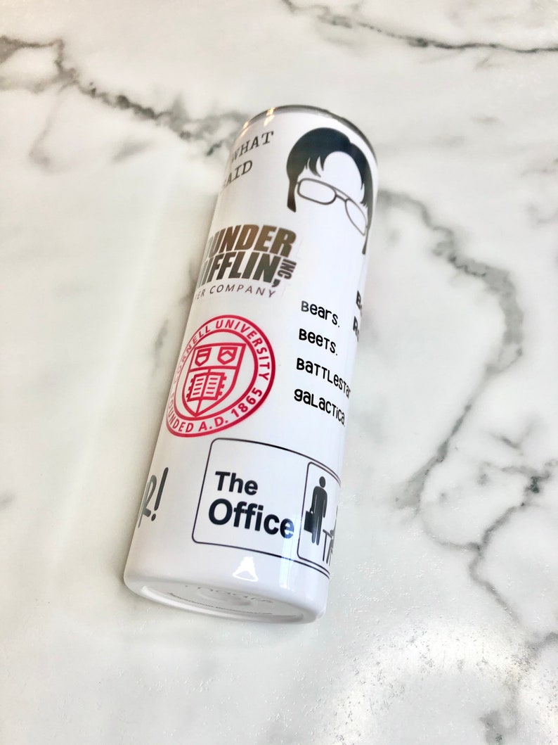 May include: White tumbler with a black and white image of a man wearing glasses. The text "Dunder Mifflin" is printed in gold on the tumbler. The text "Bears. Beets. Battlestar Galactica" is printed in black on the tumbler. The text "The Office" is printed in black on the tumbler.