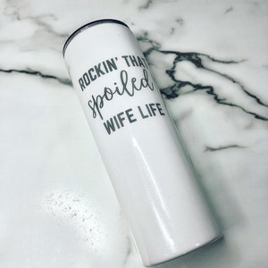 May include: White stainless steel tumbler with a silver inscription that reads "Rockin' That Spoiled Wife Life".