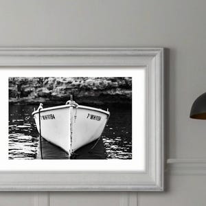 Puede incluir: Una fotografía en blanco y negro de un pequeño bote blanco con los números "7 MH1194" y "7 MH1194" pintados en el lateral, descansando en el agua.