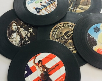 Puede incluir: Una colección de seis discos de vinilo negros con varias portadas de álbumes, incluyendo Surfer Girl de The Beach Boys, Bob Dylan, Neil Young, Tom Petty, Bitches Brew de Miles Davis y Born in the U.S.A. de Bruce Springsteen, dispuestos en círculo.