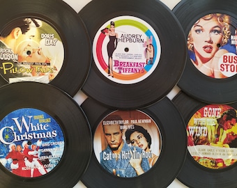 May include: Six black vinyl record coasters featuring movie posters. The coasters feature Audrey Hepburn in "Breakfast at Tiffany's", Doris Day in "Pillow Talk", Rock Hudson in "Pillow Talk", Marilyn Monroe in "Bus Stop", Elizabeth Taylor and Paul Newman in "Cat on a Hot Tin Roof", and Clark Gable and Vivien Leigh in "Gone With the Wind".