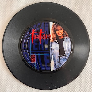 Op de afbeelding: Een zwarte vinylplaat met Tina Turner. Het label van de plaat heeft de tekst "Tina Turner" in het rood en de woorden "Break Every Rule" in het blauw. Een foto van Tina Turner staat aan de rechterkant van het label.