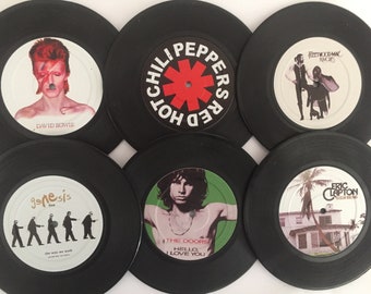 Puede incluir: Seis discos de vinilo negros con etiquetas centrales de David Bowie, Red Hot Chili Peppers, Fleetwood Mac Rumours, Genesis Live The Way We Walk, The Doors Hello I Love You y Eric Clapton 461 Ocean Boulevard dispuestos en dos filas de tres.