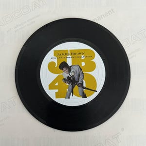May include: A black vinyl record with a white label featuring a photo of James Brown in a black suit and a white shirt. The label also includes the text "JAMES BROWN 40TH ANNIVERSARY COLLECTION" in yellow letters.