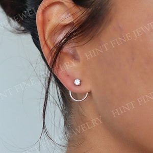 May include: A close-up of a person's ear with a small diamond stud earring and a silver hoop earring. The earrings are simple and elegant.