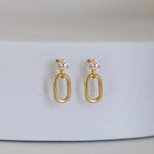 May include: A pair of gold earrings with a small clear stone at the top and a dangling oval link.