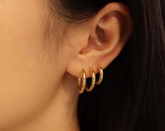 May include: A person wearing three gold hoop earrings in their left ear. The earrings are different sizes, with the largest hoop being on the bottom and the smallest hoop on the top.