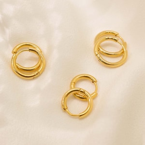 May include: Three pairs of gold hoop earrings of different sizes. The earrings are on a white background.
