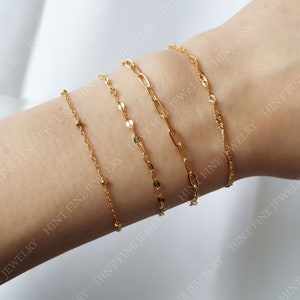 May include: Four gold chain bracelets stacked on a person's wrist. The bracelets are different styles and thicknesses.