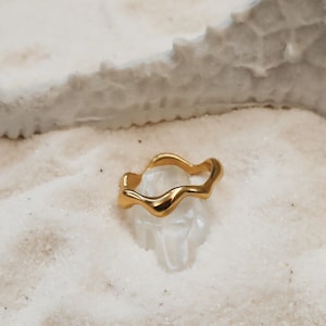May include: A gold-coloured ring with a wavy, organic design. The ring is made of metal and has a smooth, polished finish.