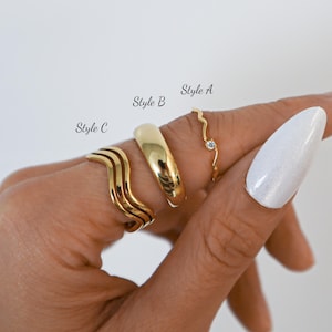 May include: Four gold rings are shown on a hand: Style A, a delicate wavy ring with a small gemstone; Style B, a smooth, rounded band; and Style C, a wavy, multi-layered ring. The rings are displayed against a light background.