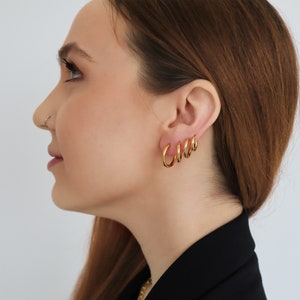 May include: A woman wearing gold hoop earrings of different sizes. The earrings are stacked on top of each other in the woman's ear.