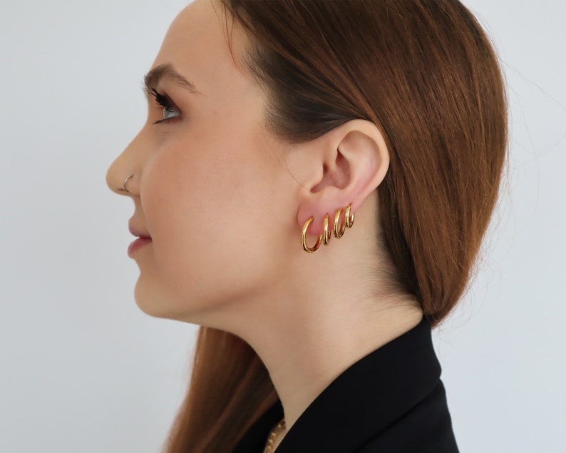 May include: A woman wearing gold hoop earrings of different sizes. The earrings are stacked on top of each other in the woman's ear.