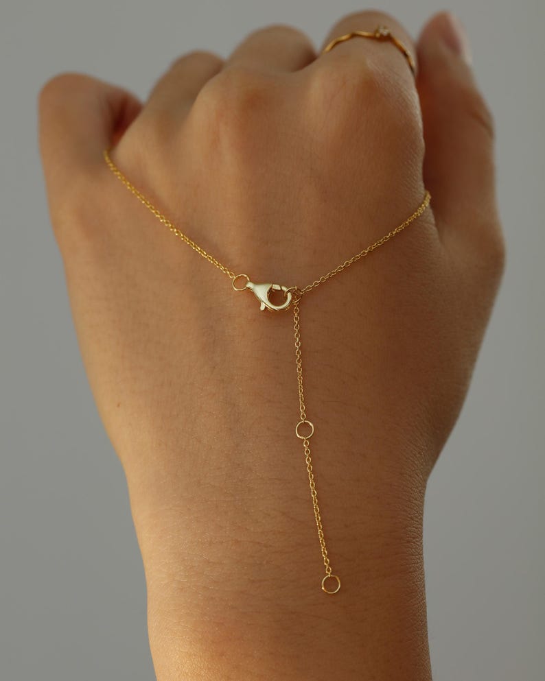 May include: A delicate gold necklace with a lobster clasp and an adjustable chain. The necklace features a fine chain with a small pendant and a simple, elegant design. The jewelry is displayed against a neutral background.