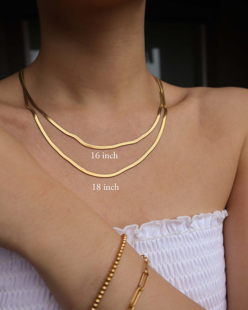 May include: Two gold chain necklaces, one 16 inches long and the other 18 inches long, are layered on a person's neck. The necklaces are made of a thin, delicate chain.