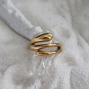 May include: A gold-toned ring with a unique, abstract design. The ring is made of three intertwined bands of metal, creating a modern and minimalist look.