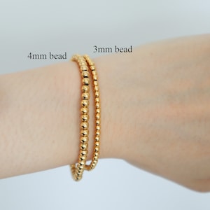 May include: Two gold bracelets on a person's wrist. The bracelet on the top is 4mm in diameter and the bracelet on the bottom is 3mm in diameter.