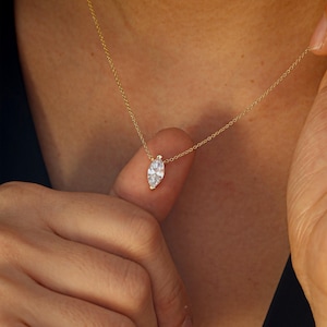 May include: A delicate gold necklace featuring a marquise-cut diamond pendant. The pendant is a clear, sparkling gemstone suspended from a thin gold chain. The necklace is shown against a neutral background.