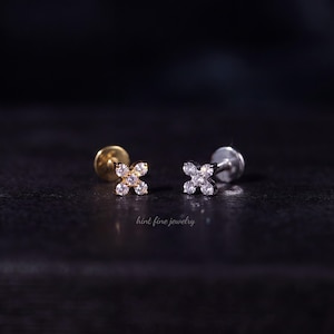 May include: Two stud earrings featuring a four-petaled flower design, each set with four small clear round-cut stones. One earring is gold-toned and the other is silver-toned, both with a flat back post. The text hint fine jewelry is visible.