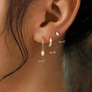 May include: Three gold-toned earrings featuring marquise-cut clear stones. Style A is a small hoop with a dangling stone. Style B is a curved stud with three stones. Style C is a single marquise-cut stone stud. The text labels A, B, and C are visible.