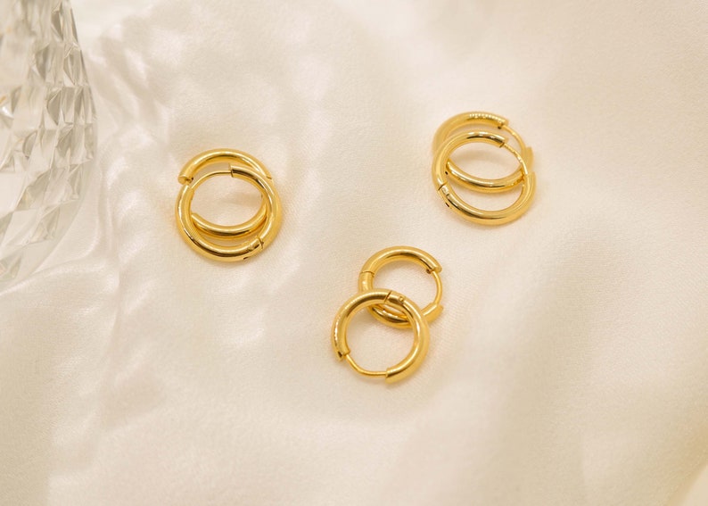 May include: Three pairs of gold hoop earrings of different sizes. The earrings are on a white background.