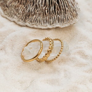 Peut inclure: Trois bagues en or empilées les unes sur les autres. La bague du haut est une bague perlée, la bague du milieu est une bague à maillons carrés et la bague du bas est une simple bande.