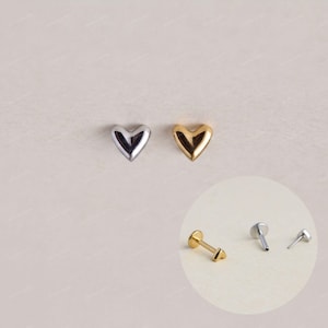 May include: Two heart-shaped stud earrings, one in silver tone and one in gold tone, are displayed. An inset shows the side profile of the gold stud with a flat back post, a silver stud with a post, and a small separate silver post component.
