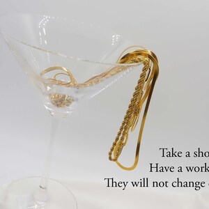 May include: A close-up of three gold chains in a martini glass. The chains are made of different styles of gold links. The text "Take a shower, Have a work out, They will not change color" is visible below the glass.