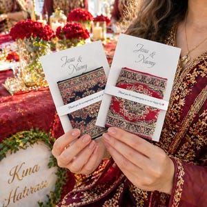May include: Two cards with the names "Jesus & Naomy" and the text "Thank you for accompanying us on our happy day". Each card holds a small, decorative textile with intricate patterns in red, blue, and gold. The background features a festive table setting.