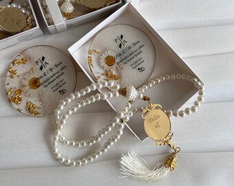May include: White gift boxes with clear lids containing small white round plates with gold accents and dried flowers. Each plate has a printed message in black text that reads "Pelin & Ali Sinan Birbirinden habersiz edilen iki duanın kabulü 30 Eylül 2023 Aşk ile Karışan". Each box also contains a white pearl prayer beads with a gold tassel and a gold charm with the text "Pelin & Ali".