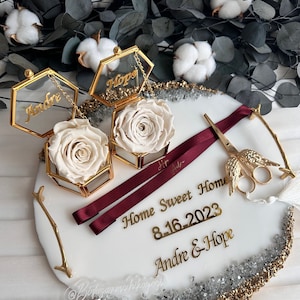 May include: White preserved roses in gold hexagonal boxes with the names "Andre" and "Hope" on the lids. The boxes are on a white resin tray with gold accents and the text "Home Sweet Home 8-16-2023 Andre & Hope".