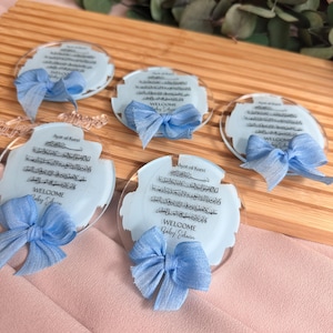 May include: Four clear acrylic circular ornaments with blue ribbon bows. Each ornament features a blue watercolor background with Arabic calligraphy and the text "Ayat al Kursi" and "WELCOME Baby Edwin".