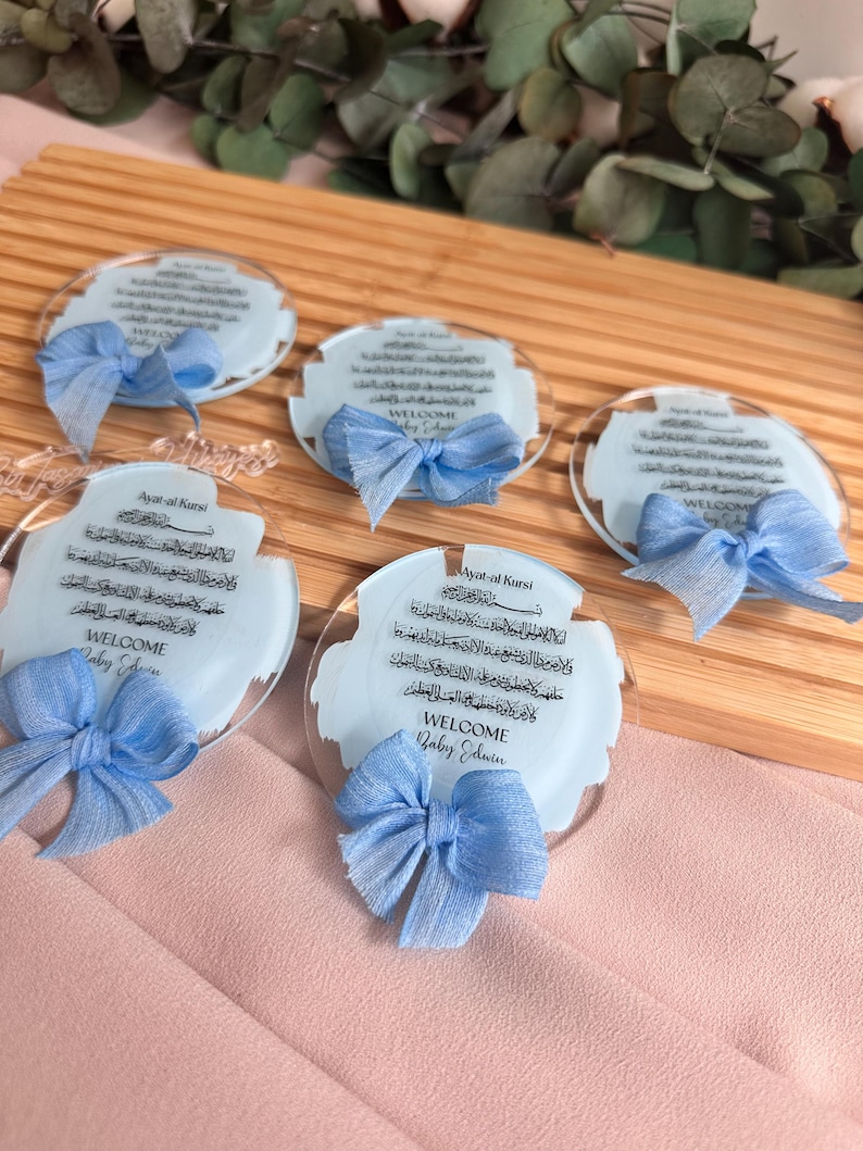 May include: Four clear acrylic circular ornaments with blue ribbon bows. Each ornament features a blue watercolor background with Arabic calligraphy and the text "Ayat al Kursi" and "WELCOME Baby Edwin".