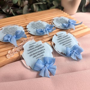 May include: Five clear acrylic plaques with blue ribbons and Arabic calligraphy. The plaques feature the text "Ayat al Kursi" and "Welcome Baby Edition".